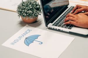 person using a computer with a piece of paper on the side with the word insurance and a photo of an umbrella printed on it